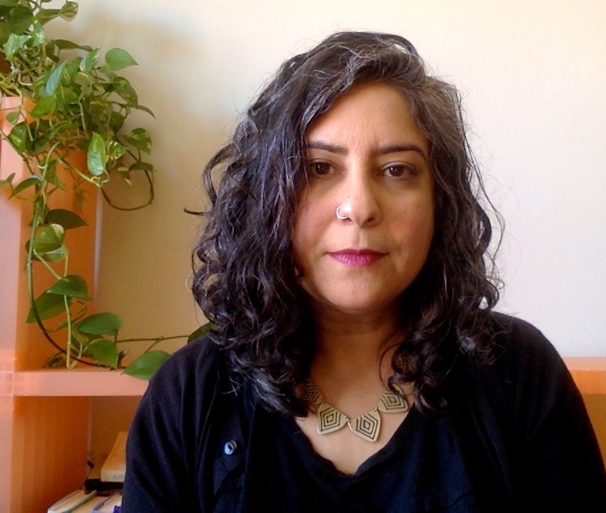 Soniya looking at the camera with a necklace on, a green vine is behind her on the left